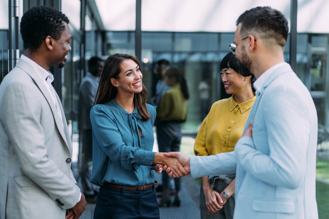 A woman shaking hand with her new employees and smiling.